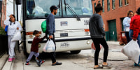 People walk in front of a parked bus to cross the street outside