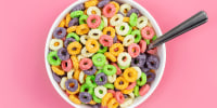 Colored breakfast cereal in a bowl on a pink background, flat lay.