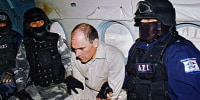 Osiel Cárdenas Guillén sitting in a plane in handcuffs between agents of Mexico's Federal Agency of Investigations